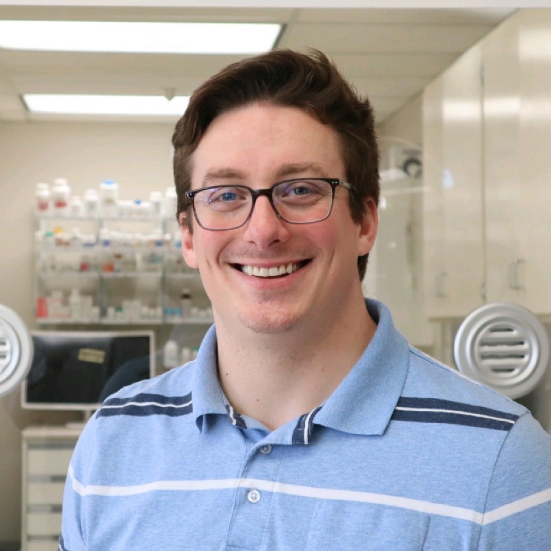 Portrait of William Herbert, PharmD, a professional multi-state licensed pharmacist specializing in sterile and non-sterile compounding, standing confidently with a friendly smile. He is wearing a white lab coat and holding a clipboard, symbolizing his dedication to quality assurance and patient safety in the pharmaceutical industry.